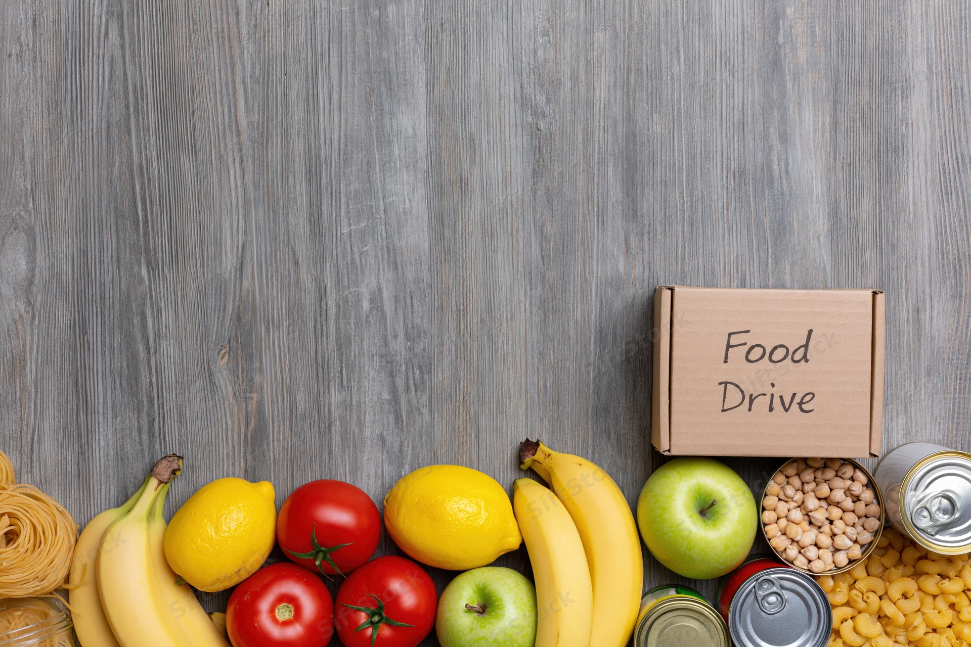 Food drive donation items arranged along the bottom of a wooden surface with copyspace above