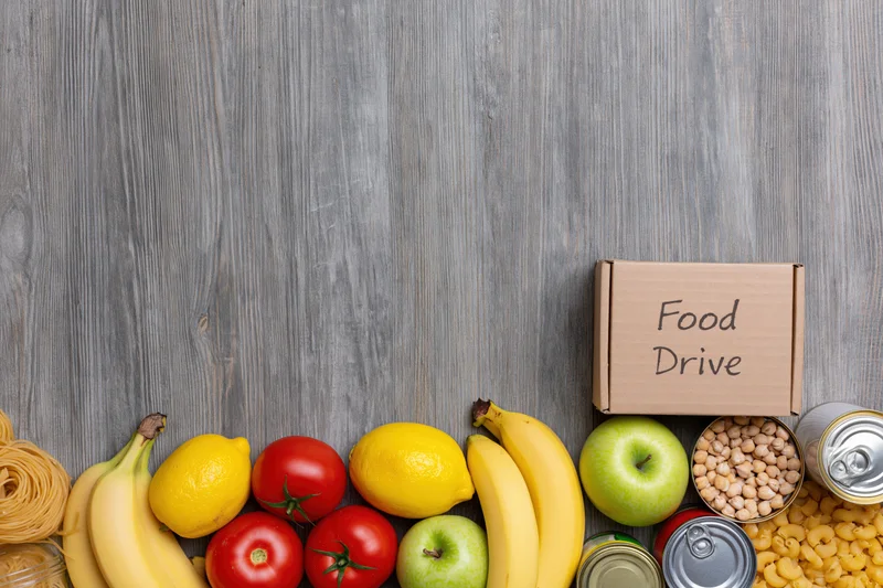 Food drive donation items arranged along the bottom of a wooden surface with copyspace above