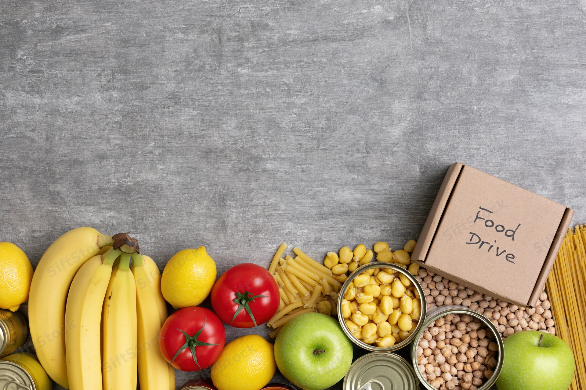 Food drive donation items arranged along the bottom of a gray surface with copyspace above
