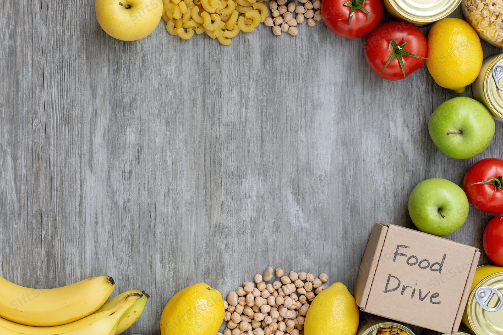 Food drive donation items arranged along the edges of a gray wooden surface with copyspace in center