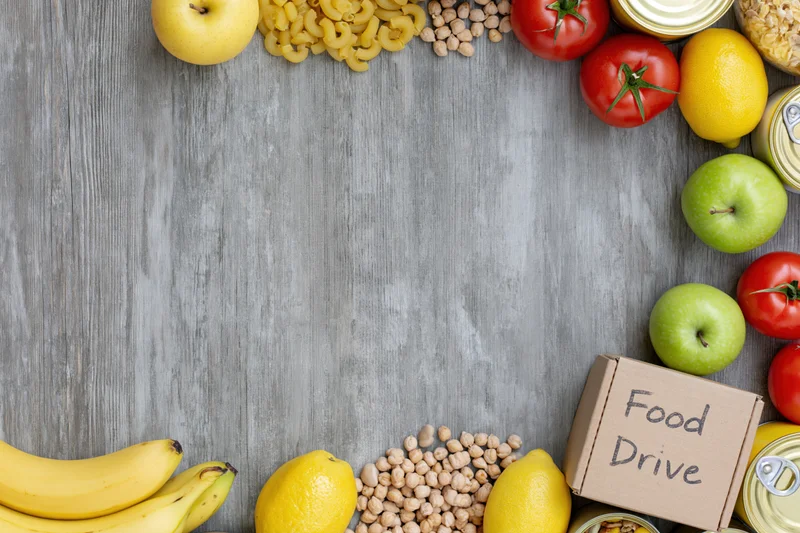 Food drive donation items arranged along the edges of a gray wooden surface with copyspace in center
