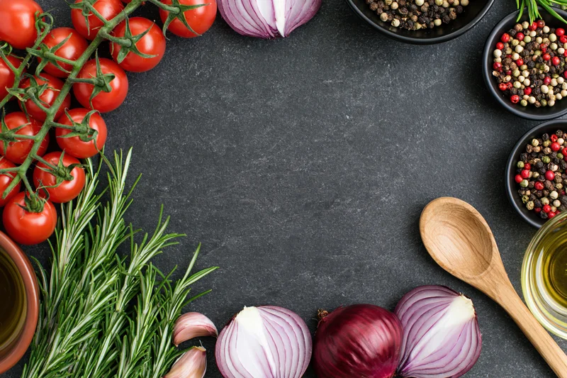 Fresh cooking ingredients arranged around the edge of a dark countertop in a flat lay with copyspace in the center