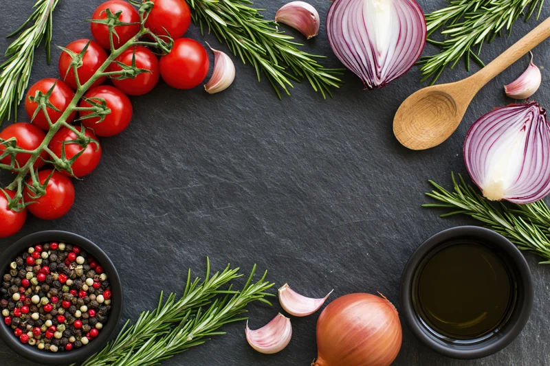 Fresh cooking ingredients arranged around the edge of a slate surface with copyspace in center
