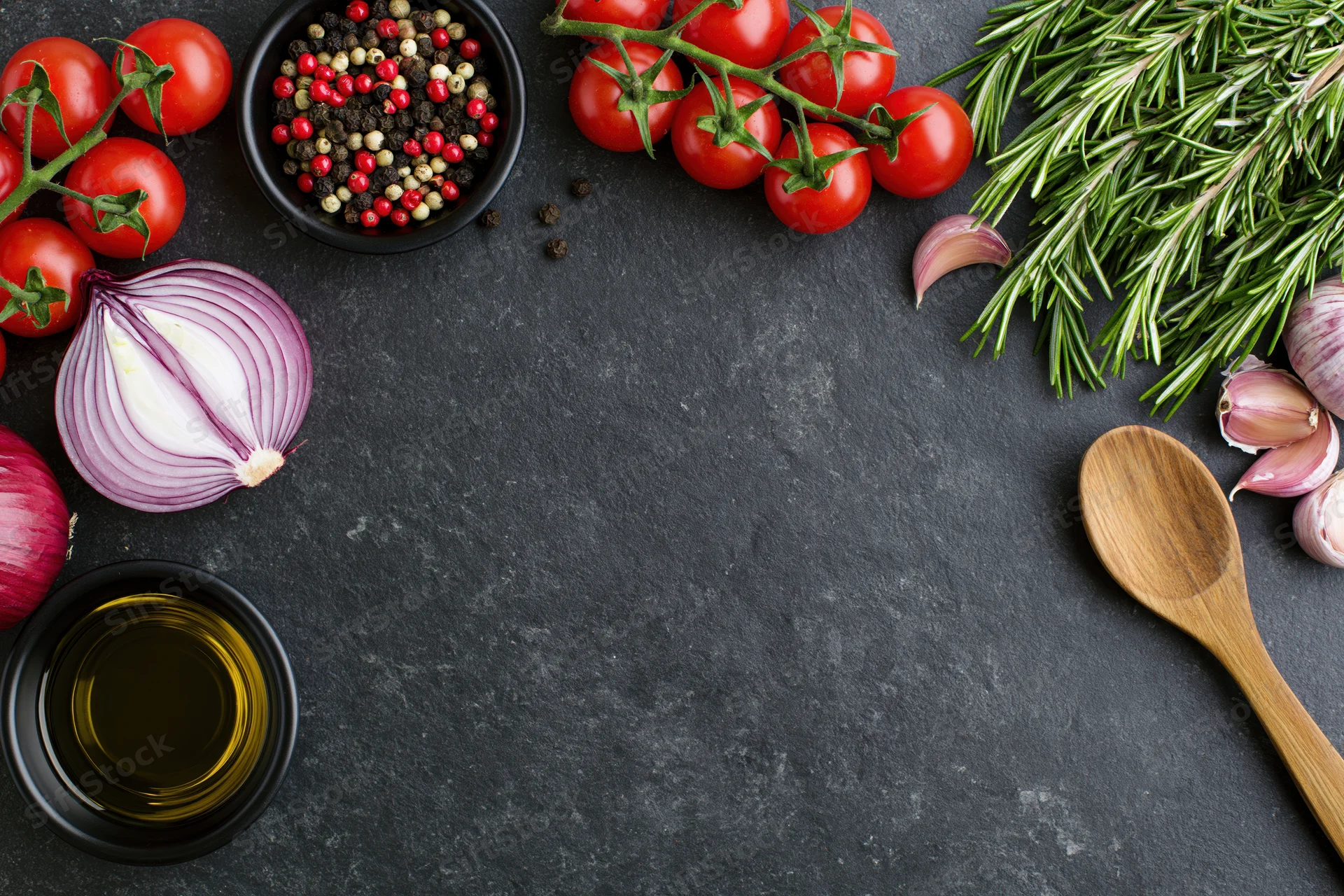 Fresh cooking ingredients arranged around the edge of a dark surface with copyspace in center