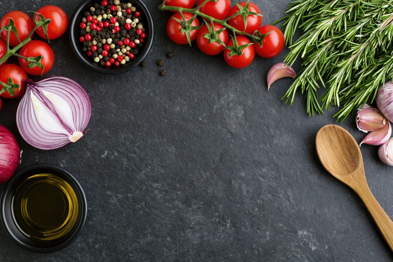 Fresh cooking ingredients arranged around the edge of a dark surface with copyspace in center
