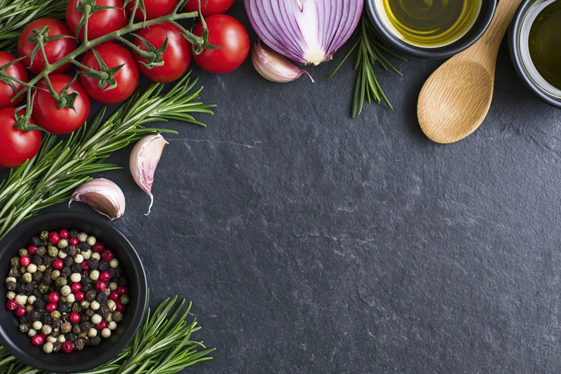 Fresh cooking ingredients arranged around the edge of a dark slate surface with copyspace in center