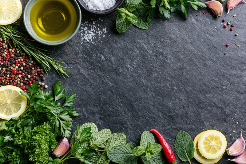 Fresh herbs and spices arranged along the edges of a dark slate surface with copyspace in center