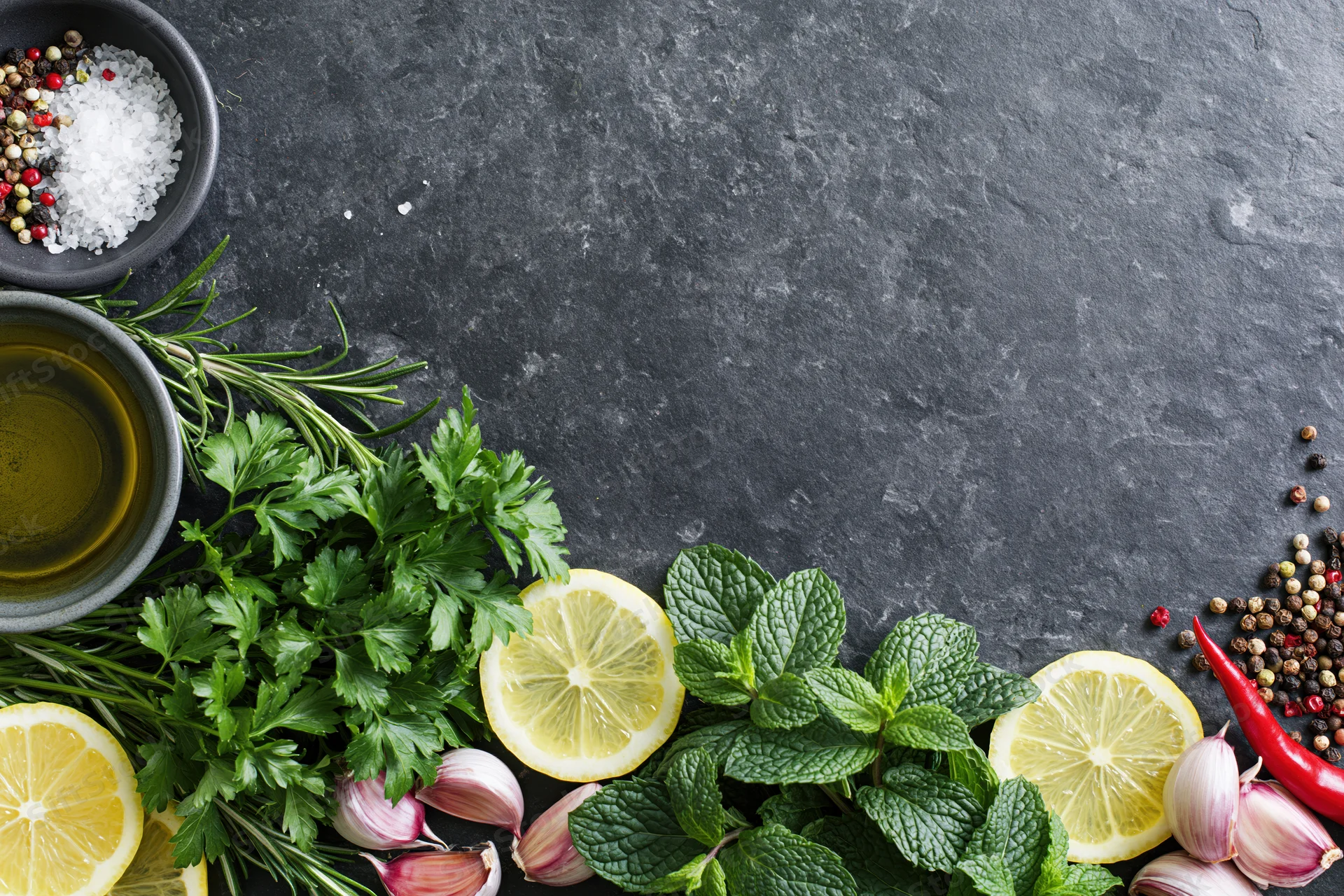 Fresh herbs and spices arranged along the edge of a dark slate countertop with copyspace
