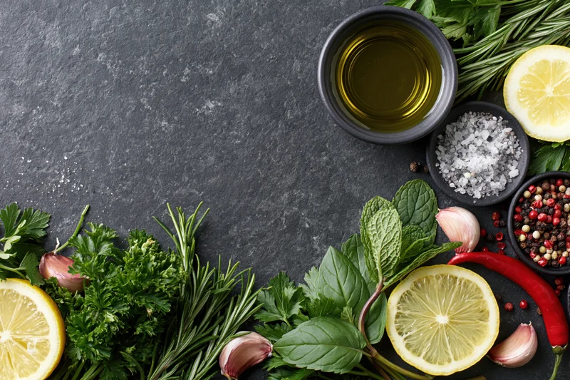 Fresh herbs and spices arranged along the bottom of a dark stone surface with copyspace above