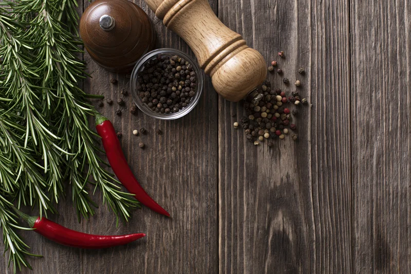 Fresh rosemary sprigs and red chili peppers with peppercorns and grinder on dark wooden table