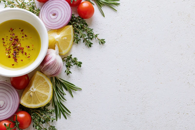 Fresh salad dressing ingredients arranged along the left side of a white textured surface with copyspace on the right