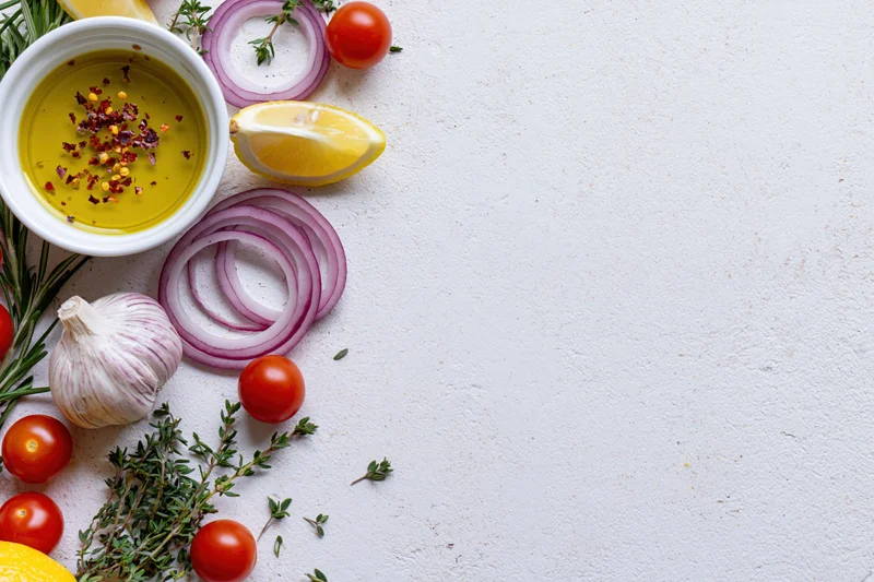 Fresh salad dressing ingredients arranged along the left side of a white countertop with copyspace on the right