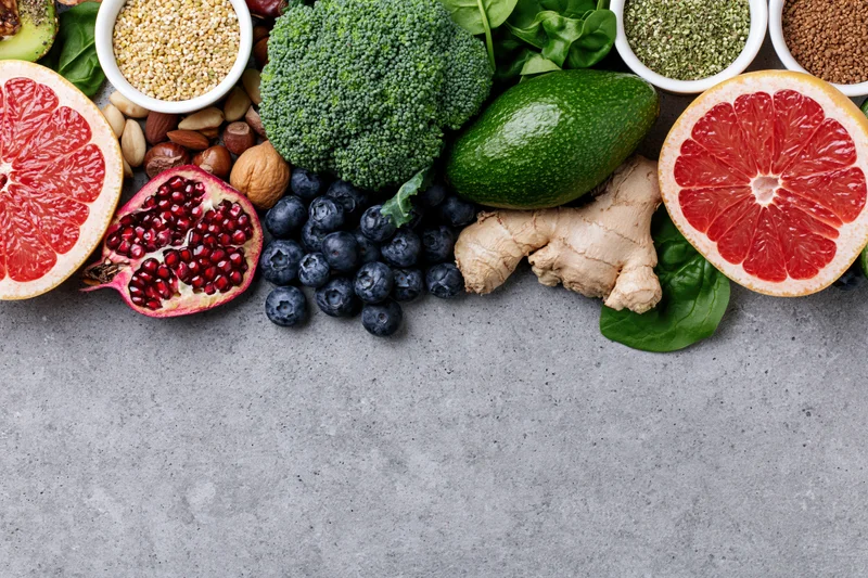 Fresh fruits vegetables nuts and seeds arranged in a flat lay on a gray countertop with copyspace