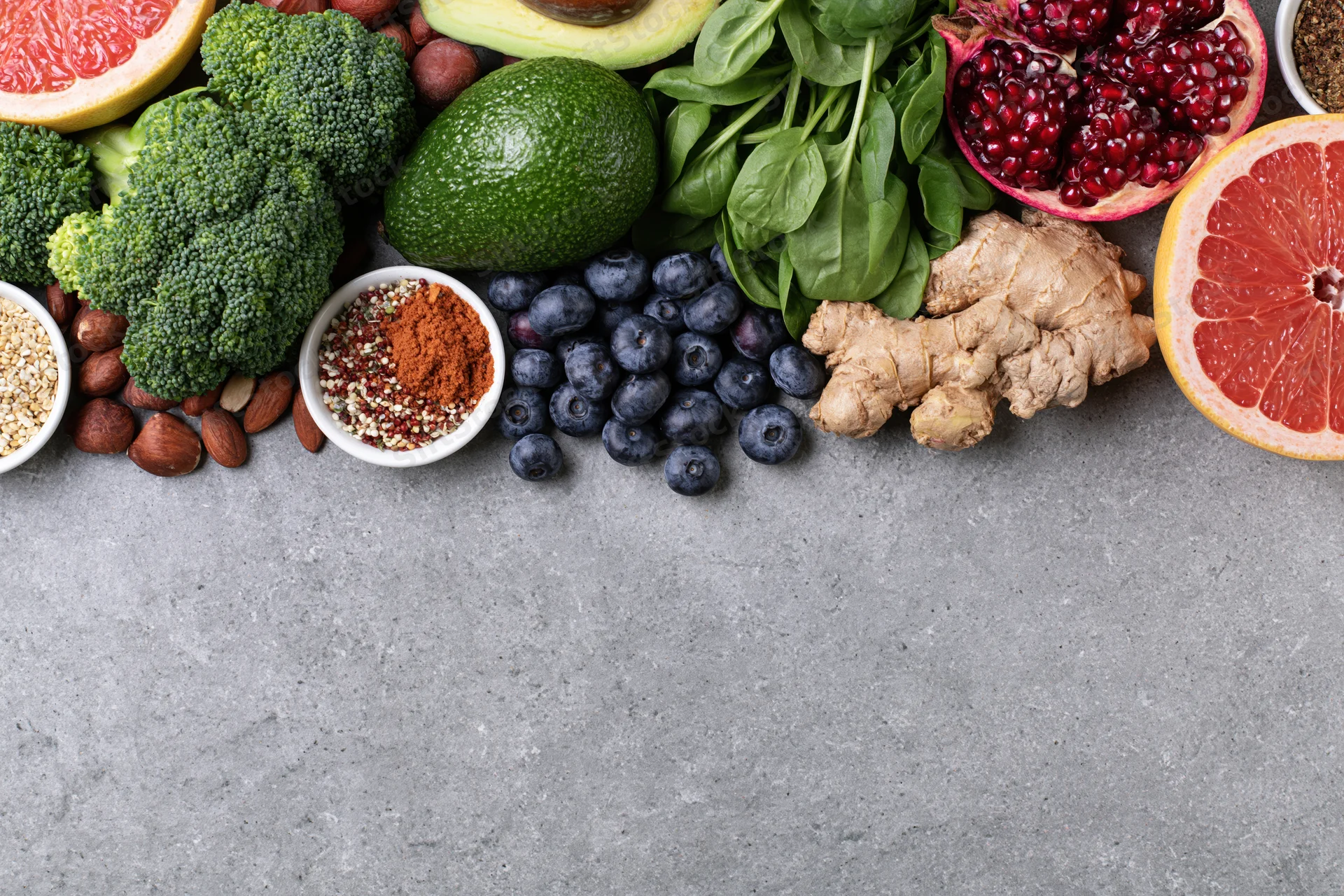 Fresh fruits vegetables nuts and seeds arranged in a flat lay on a gray surface with copyspace below