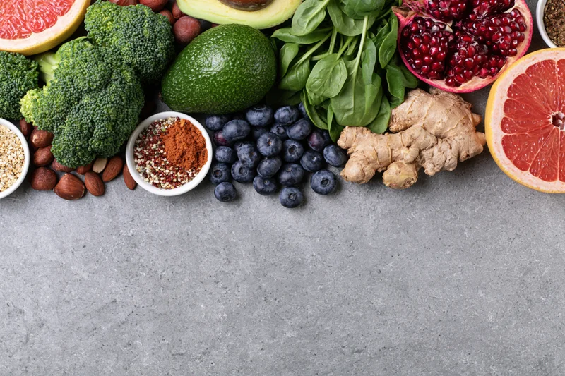 Fresh fruits vegetables nuts and seeds arranged in a flat lay on a gray surface with copyspace below
