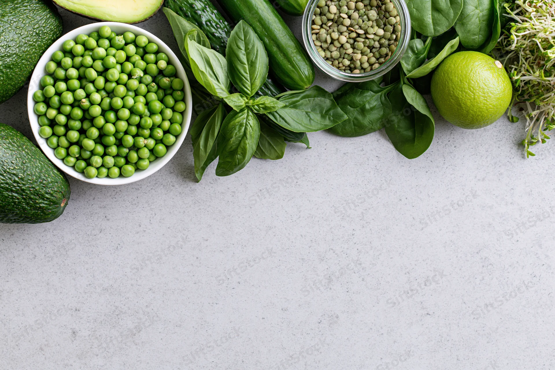 Green vegetables and ingredients arranged along the top of a gray countertop in a flat lay view