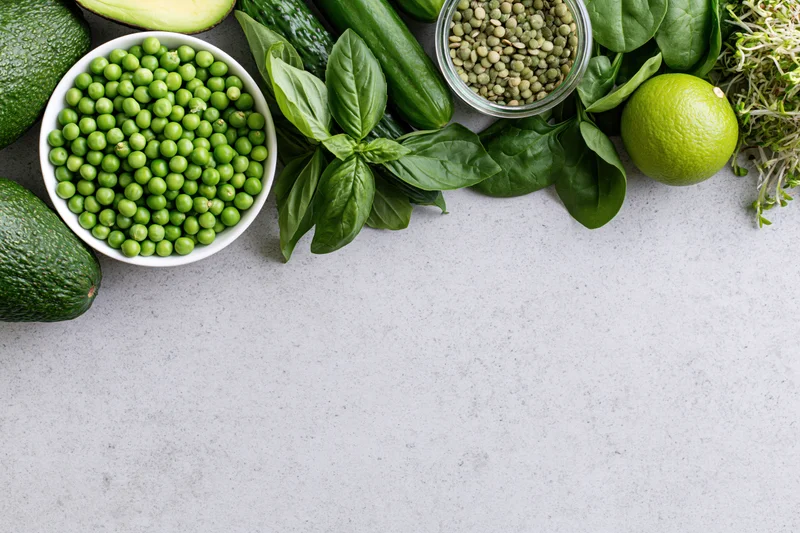 Green vegetables and ingredients arranged along the top of a gray countertop in a flat lay view
