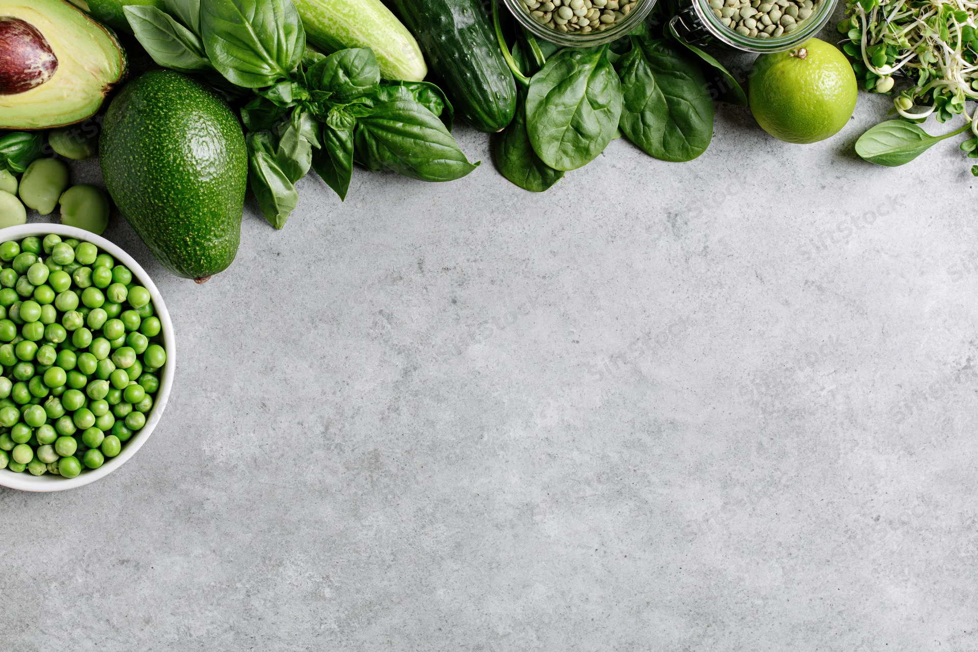 Green vegetables and ingredients arranged along the top edge of a concrete countertop with copyspace below