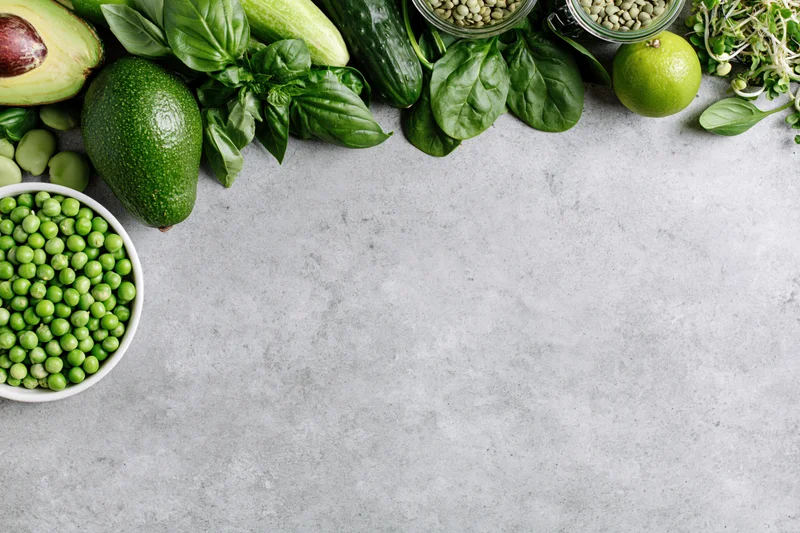 Green vegetables and ingredients arranged along the top edge of a concrete countertop with copyspace below