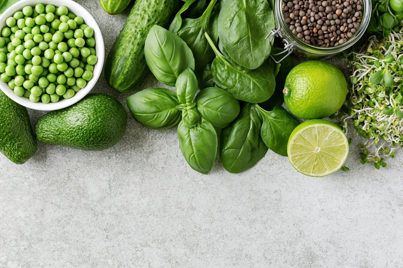 Green vegetables and ingredients arranged in a flat lay on a stone countertop with copyspace