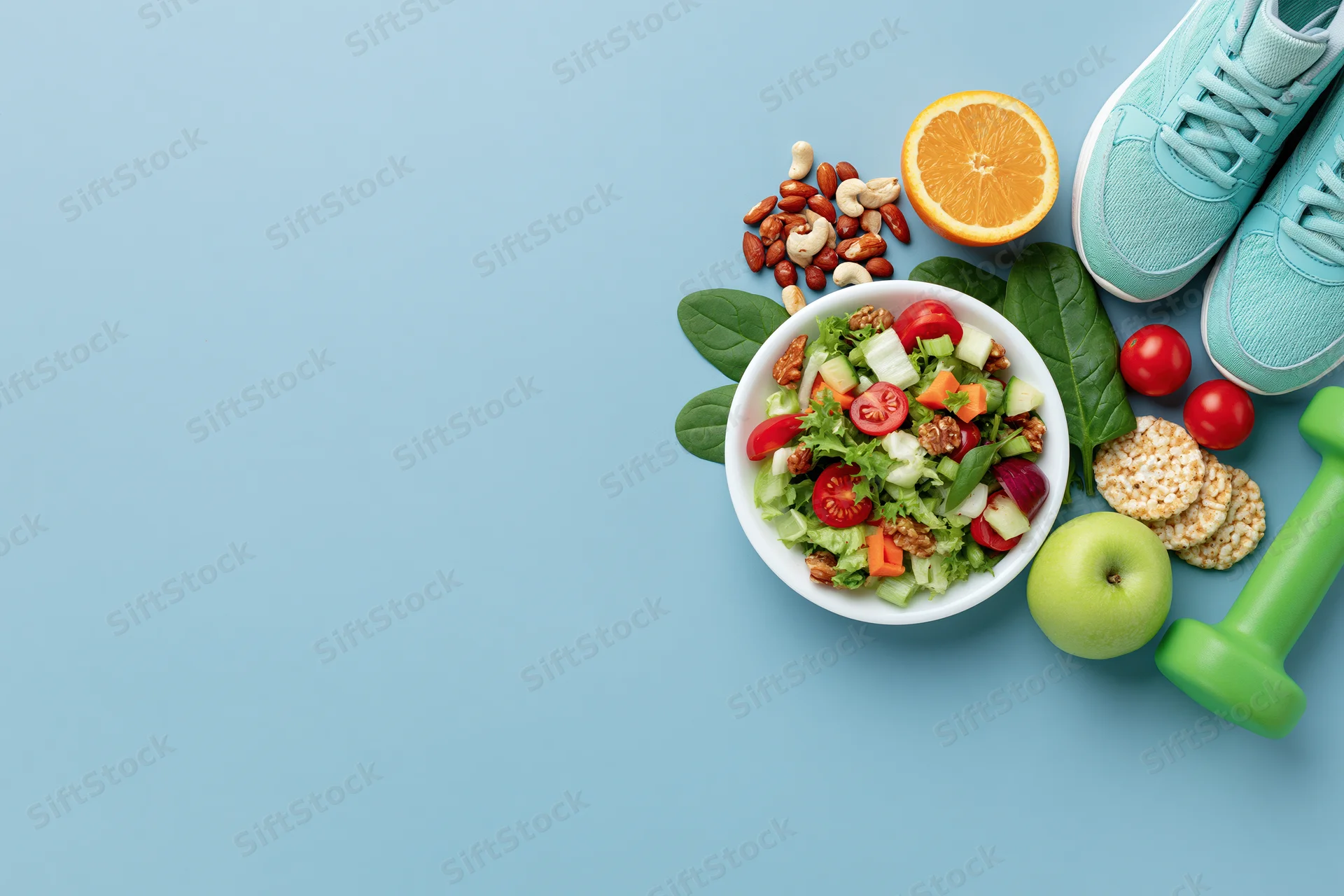 Salad with vegetables and fruit, nuts, apple, orange, sneakers and dumbbell arranged on blue background