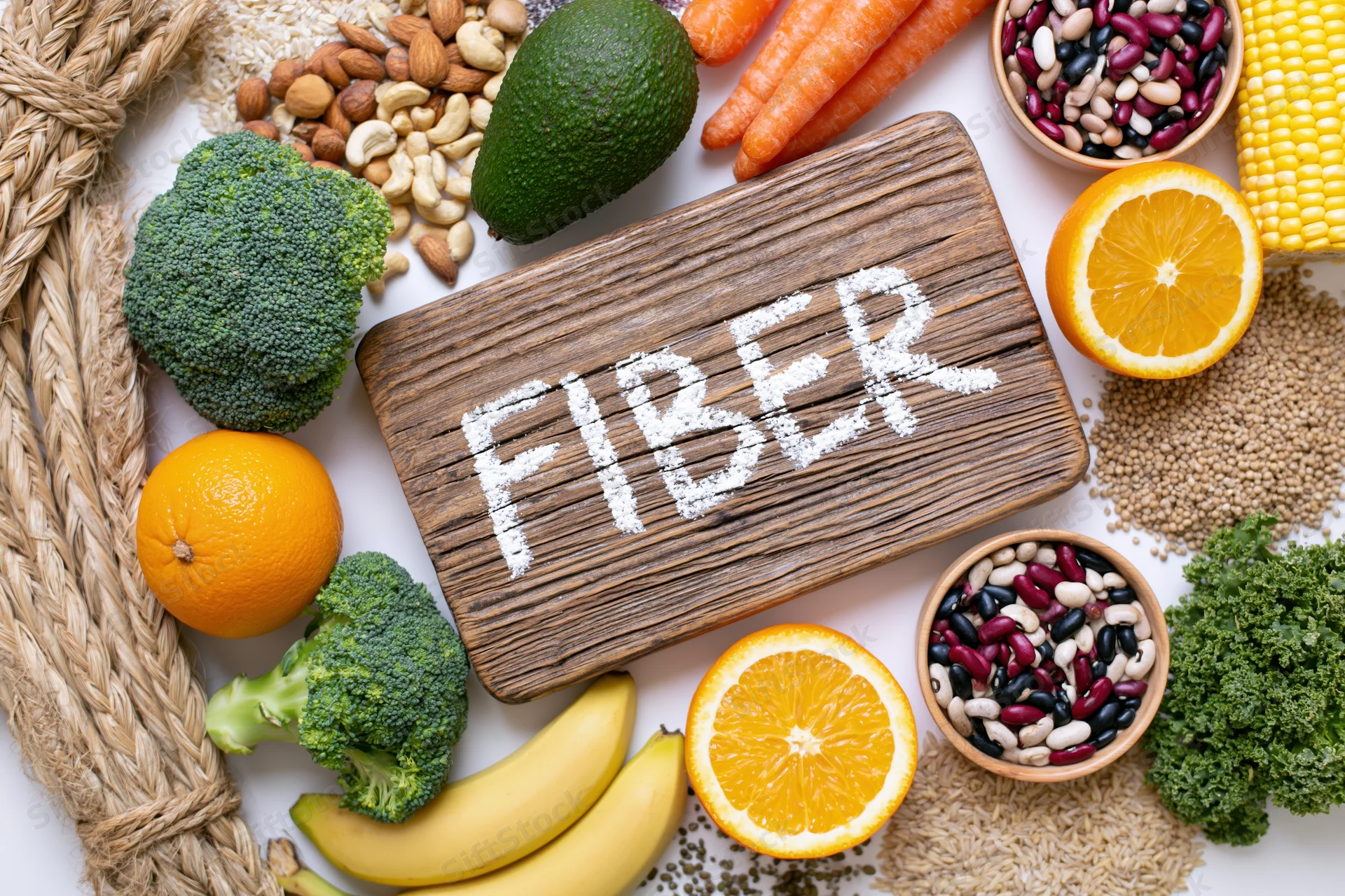 High-fiber foods arranged around a wooden board with fiber written in powder on it