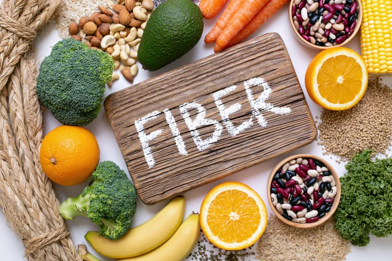 High-fiber foods arranged around a wooden board with fiber written in powder on it