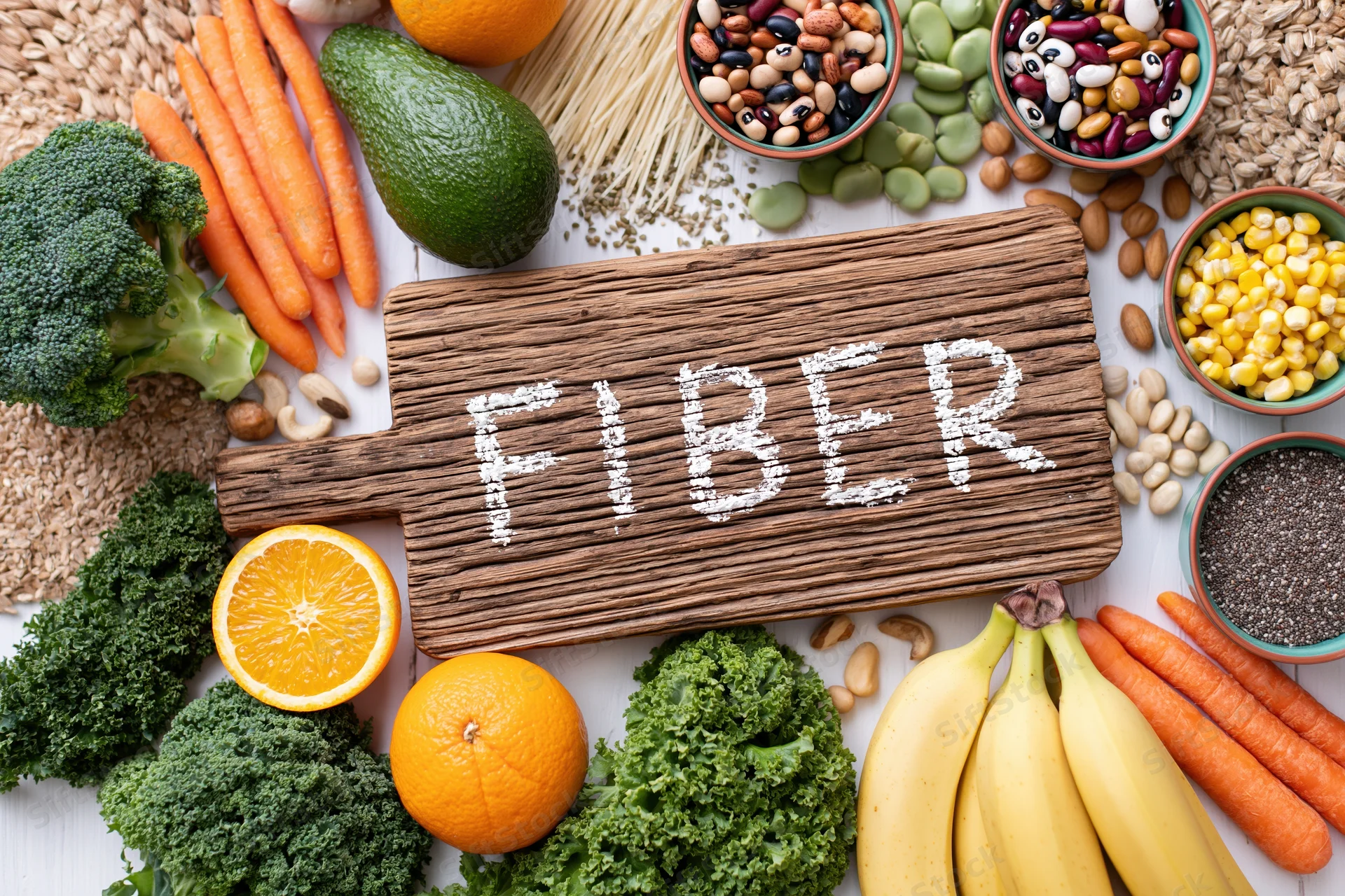High-fiber foods arranged around a wooden cutting board with fiber written in powder on it