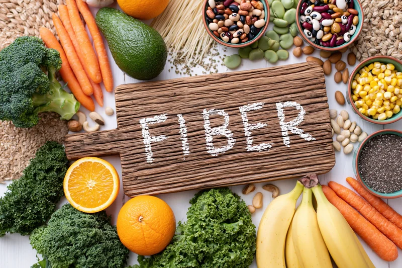 High-fiber foods arranged around a wooden cutting board with fiber written in powder on it