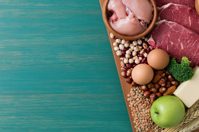 High-protein foods arranged along the right edge of a wooden board on a blue surface