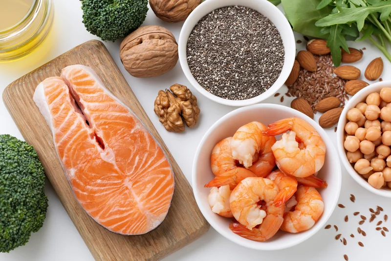 Salmon fillet and shrimp with chia seeds, broccoli, nuts and chickpeas arranged on white surface in flat lay overhead view