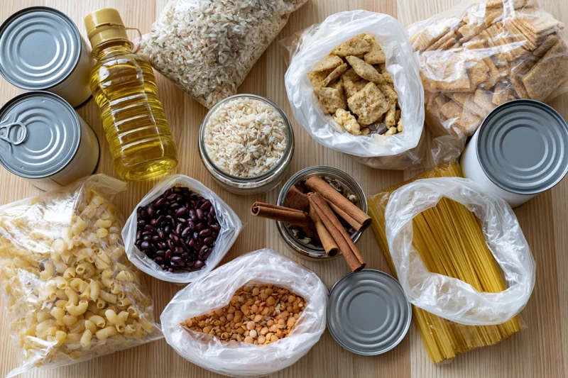 Variety of pantry staples and emergency food supplies arranged on wooden surface in flat lay view