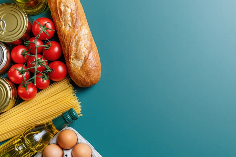 Pantry staples arranged along left edge on teal surface with copyspace