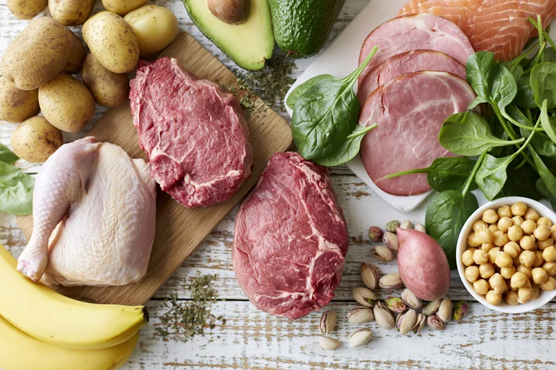 Raw protein-rich foods and fresh produce arranged on a wooden surface in a flat lay composition