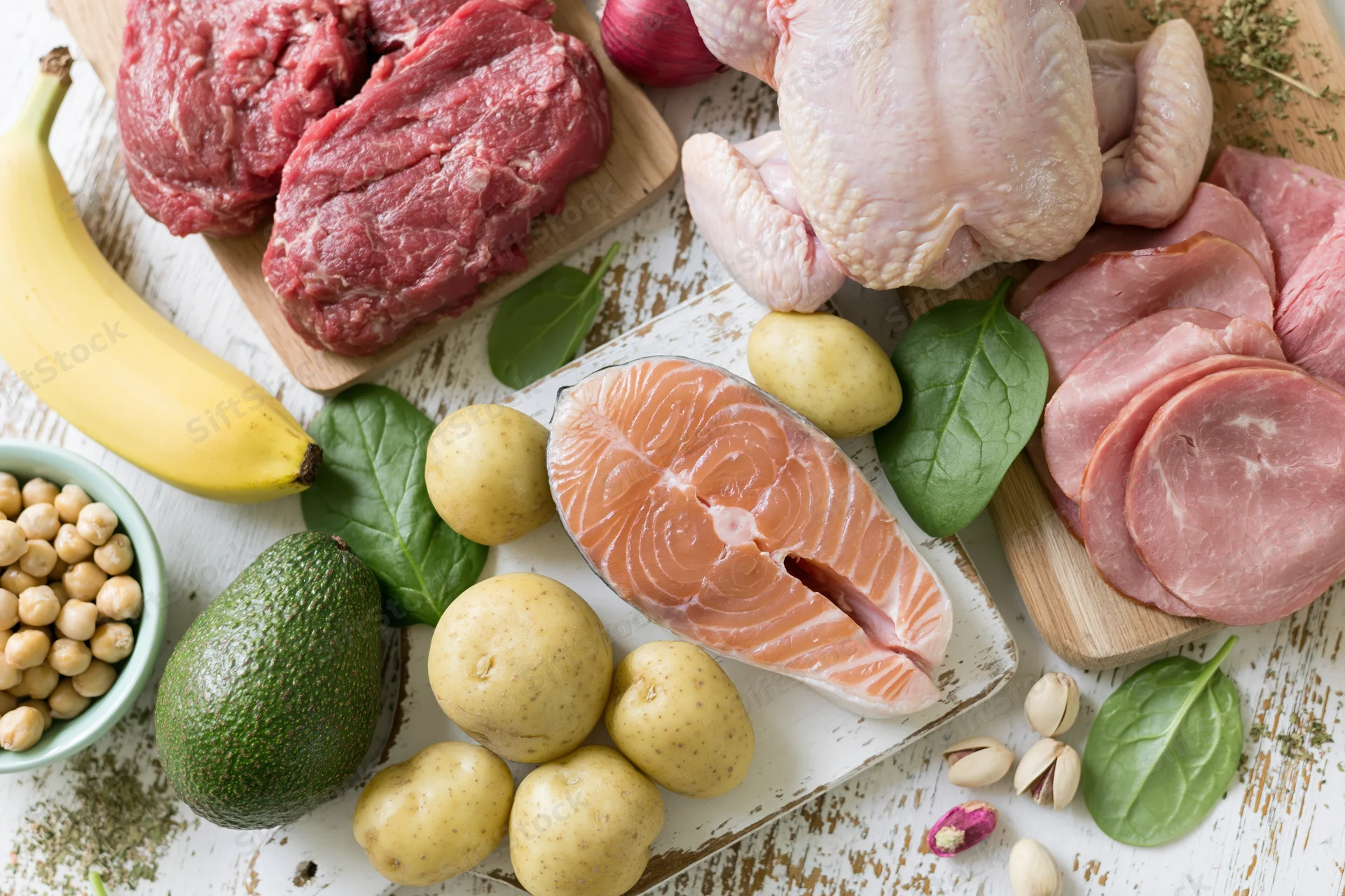 Raw protein-rich foods and fresh produce arranged on a rustic white wooden table