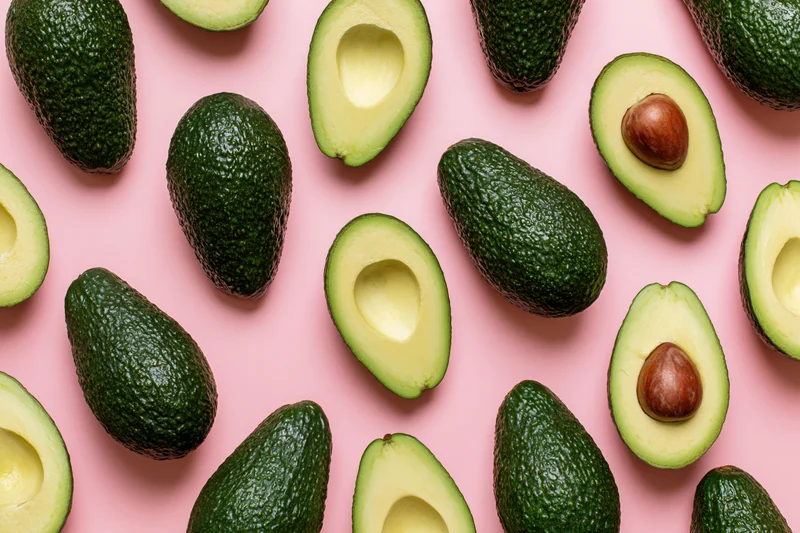 Whole and halved avocados arranged in a repeating pattern on a pink background