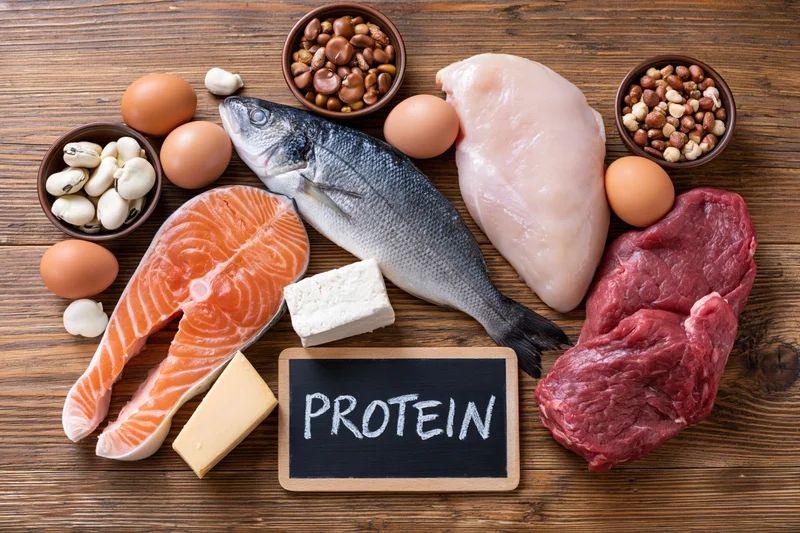 Assorted high-protein foods arranged on wooden table with chalkboard sign reading protein