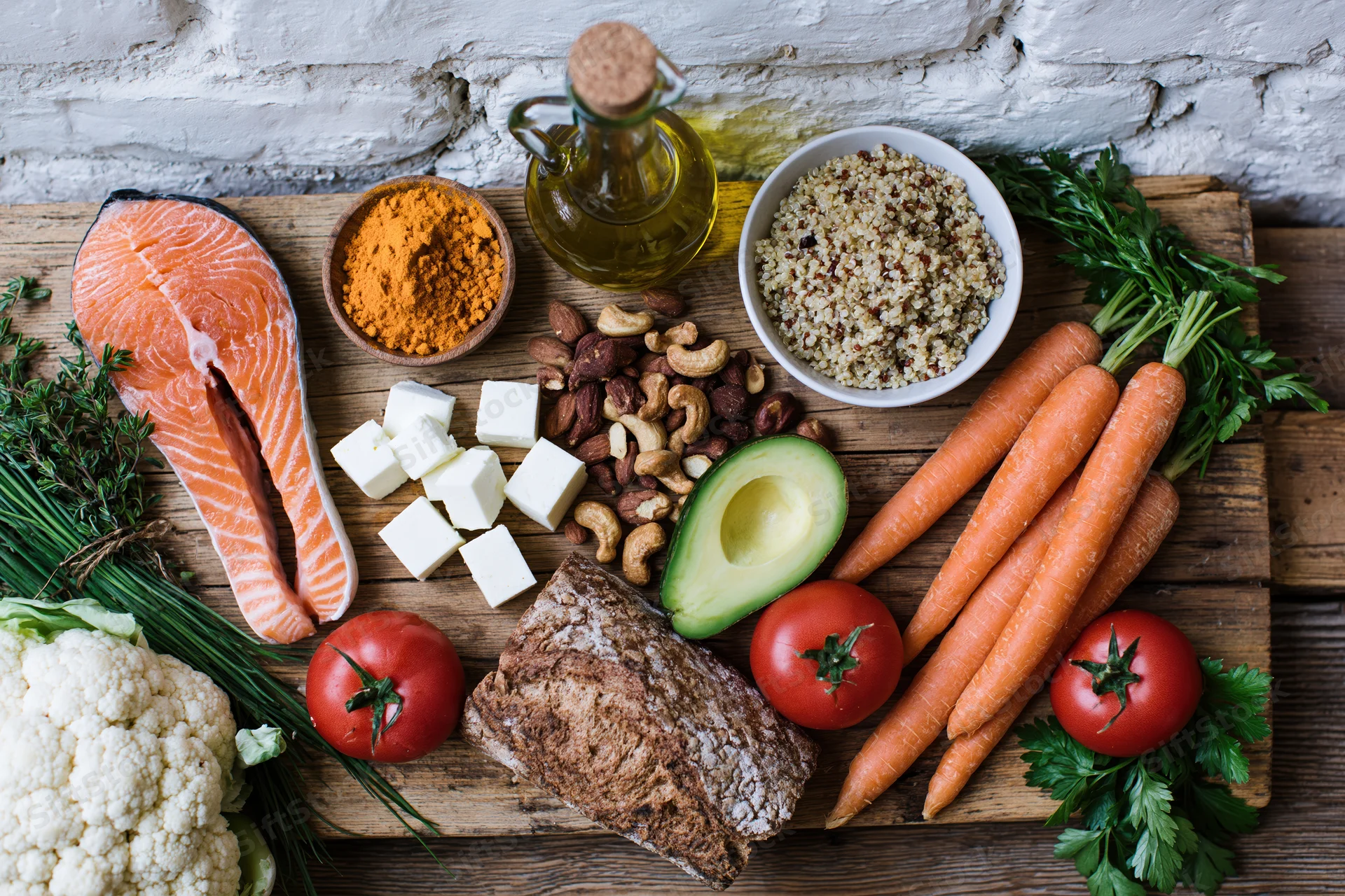 Variety of mediterranean diet ingredients arranged on a wooden board with salmon, vegetables, nuts, cheese, olive oil and herbs