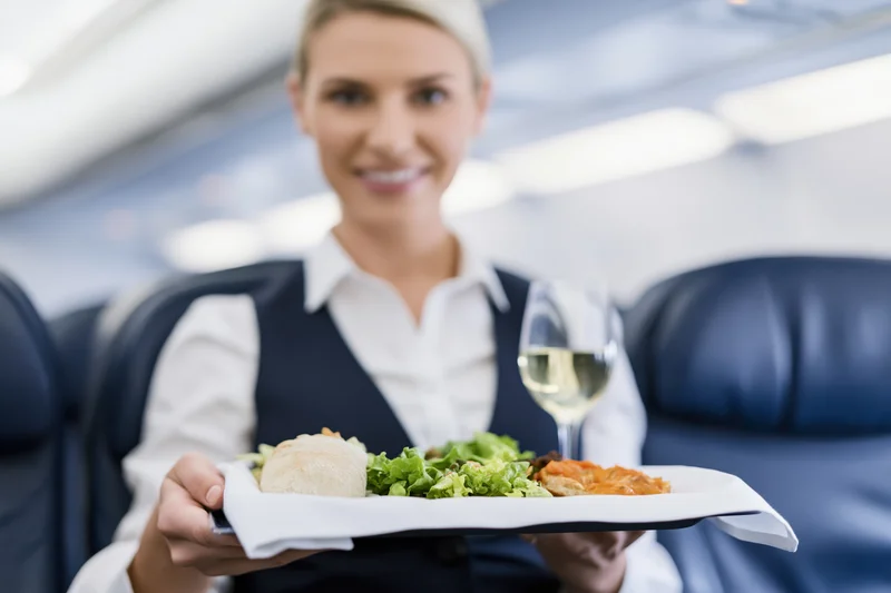 Flight attendant holding a meal service tray with food and wine in airplane cabin