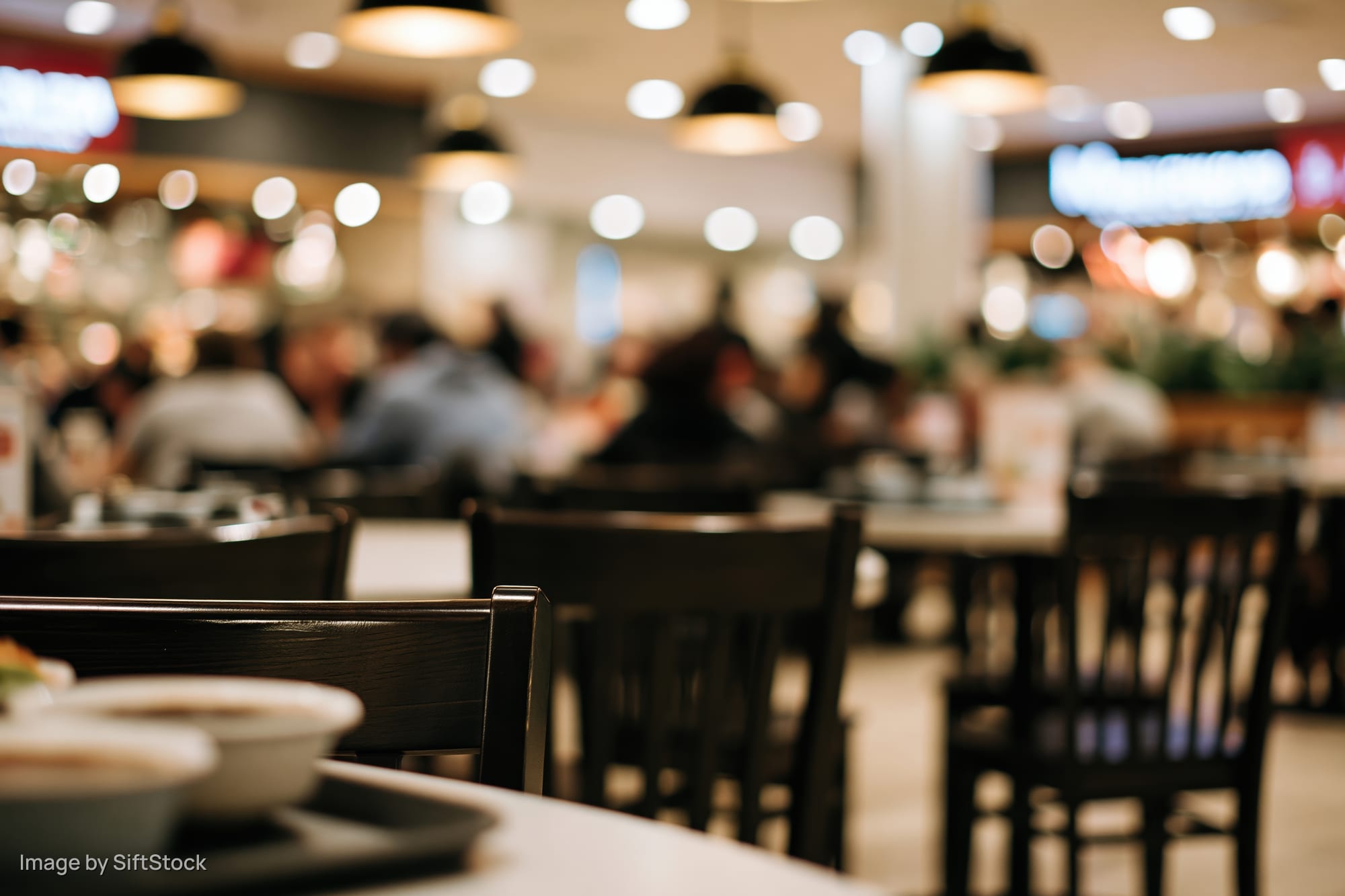 Low-angle view of dark wooden chairs and tables in a busy food court dining area