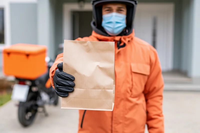 Delivery courier holding paper food bag in residential driveway