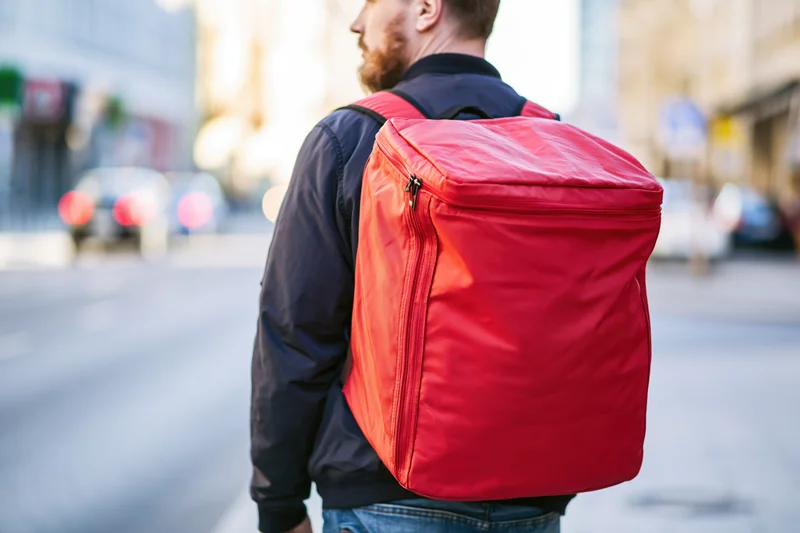 Man with red delivery backpack walking on city street