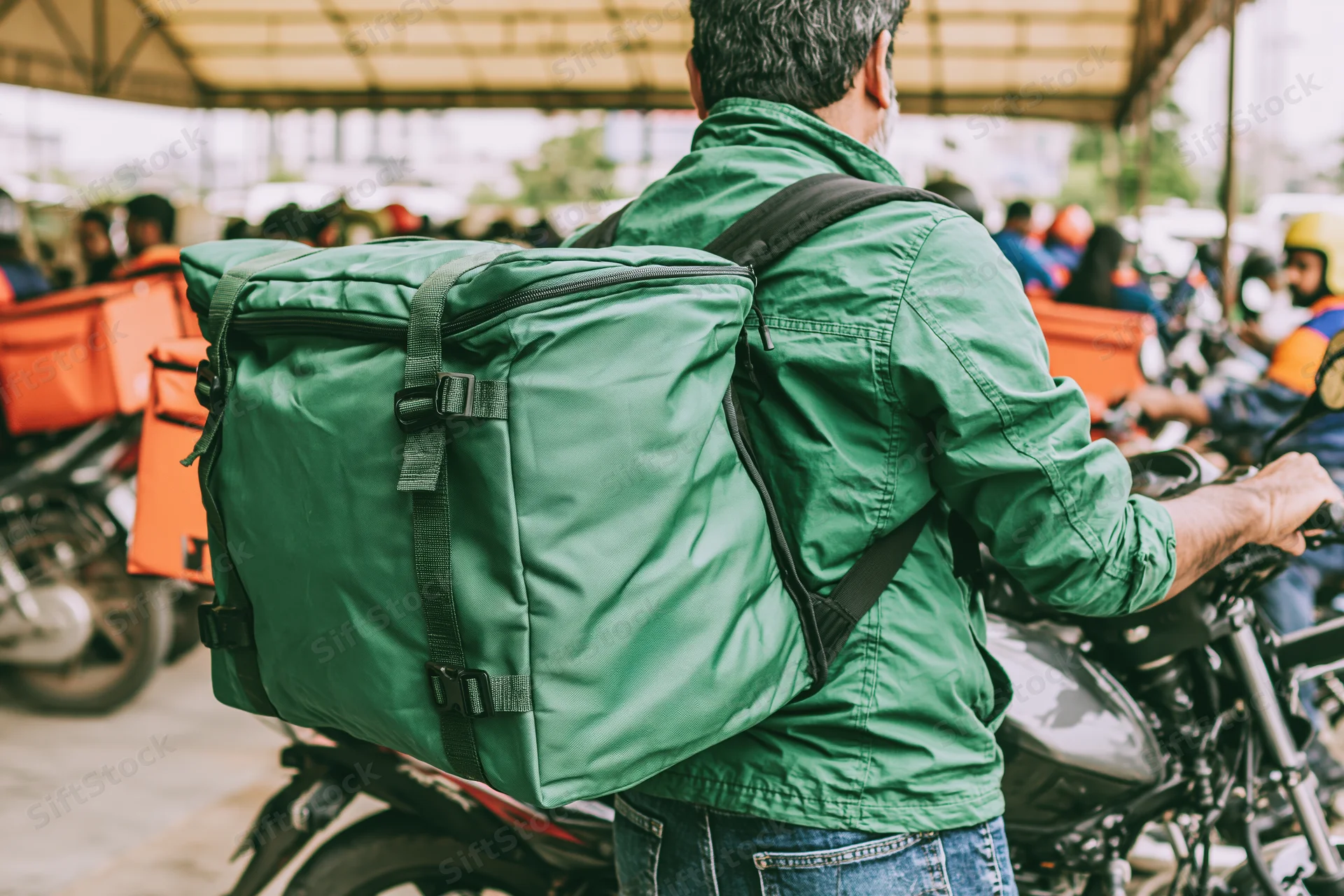 Delivery rider in green jacket with large green backpack on motorcycle in urban setting