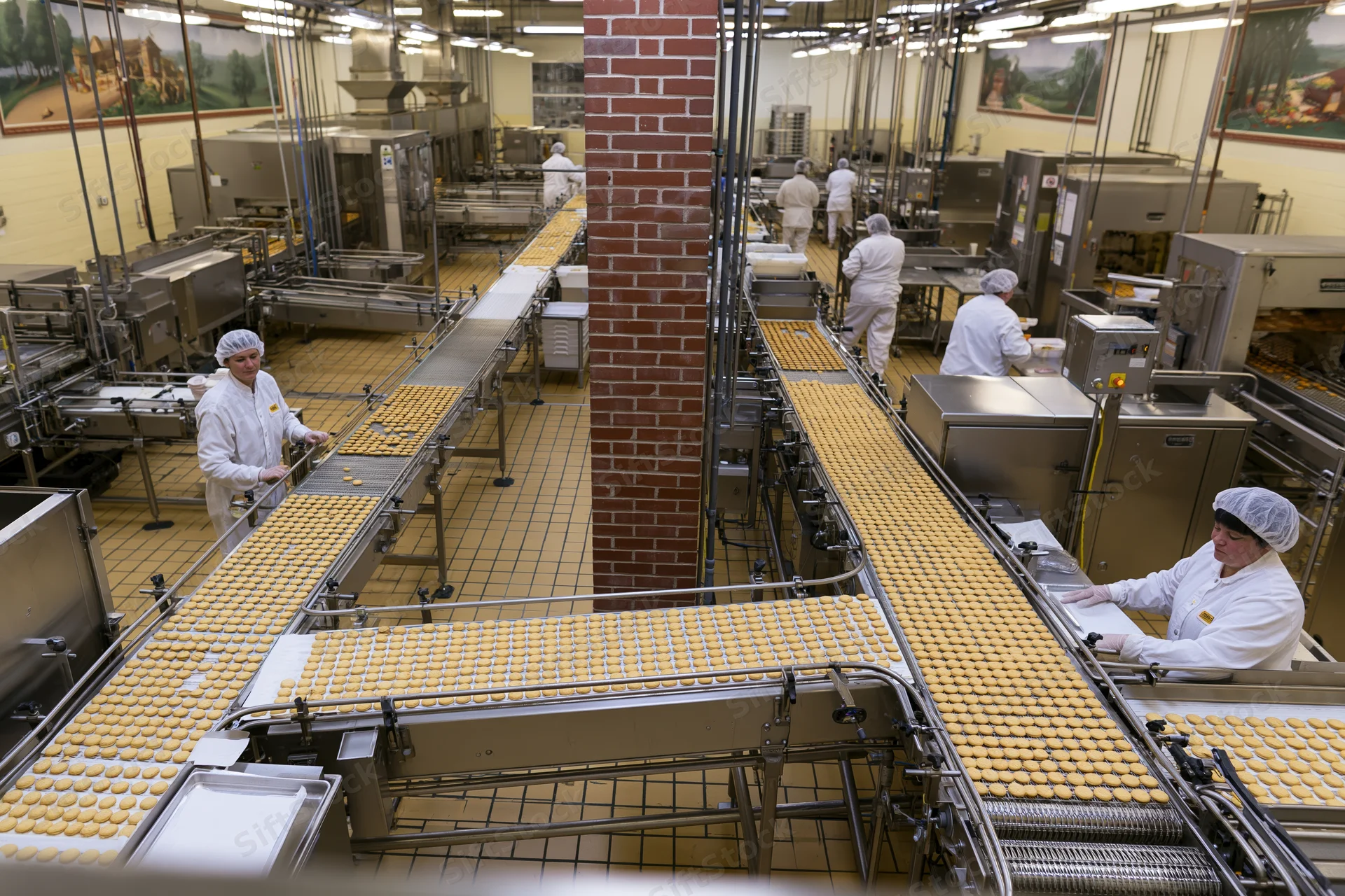 Bakery production line with workers in white uniforms handling cookies on conveyor belts inside a factory