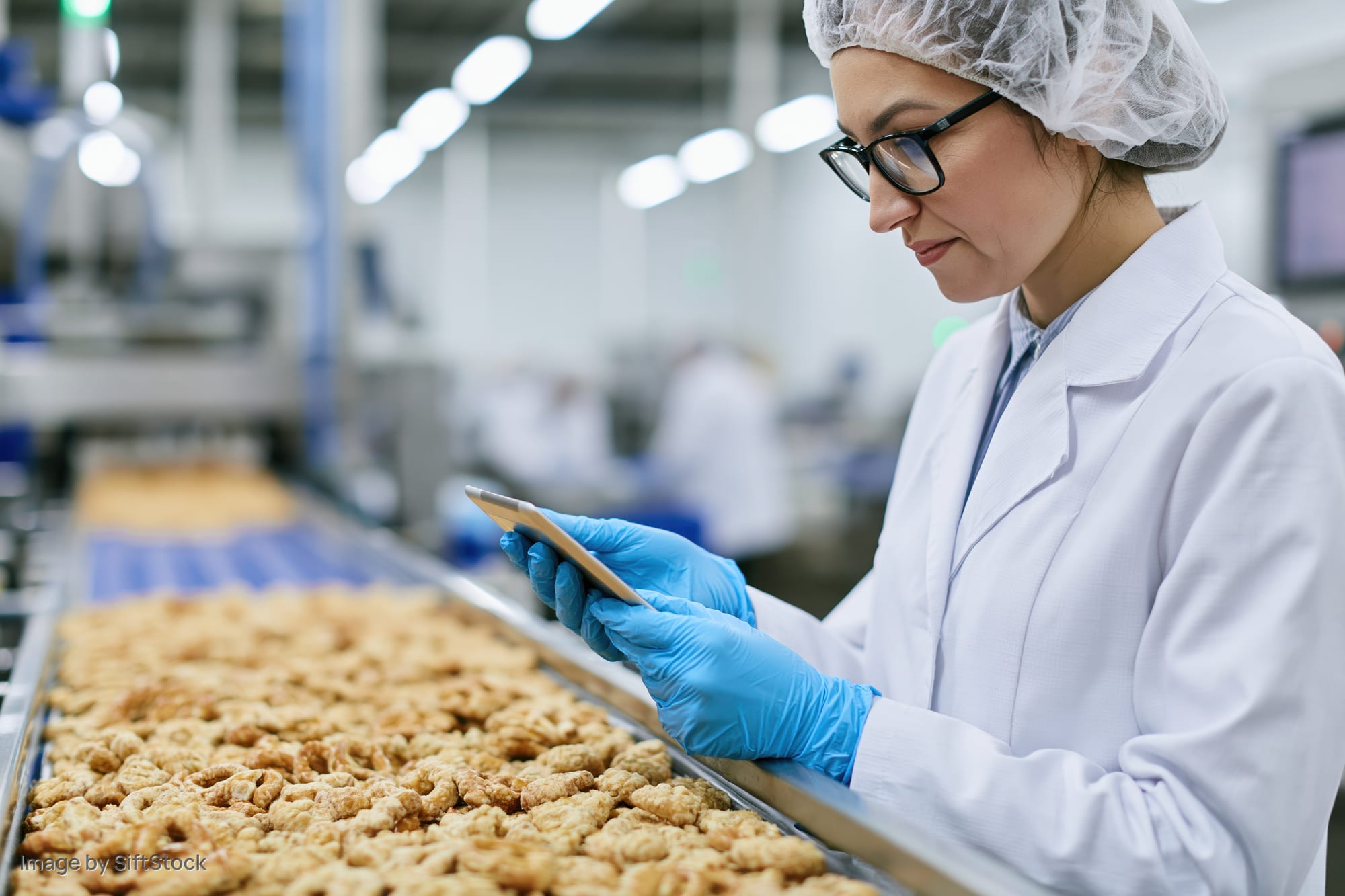 Woman in lab coat and hairnet inspecting snacks on conveyor in food factory