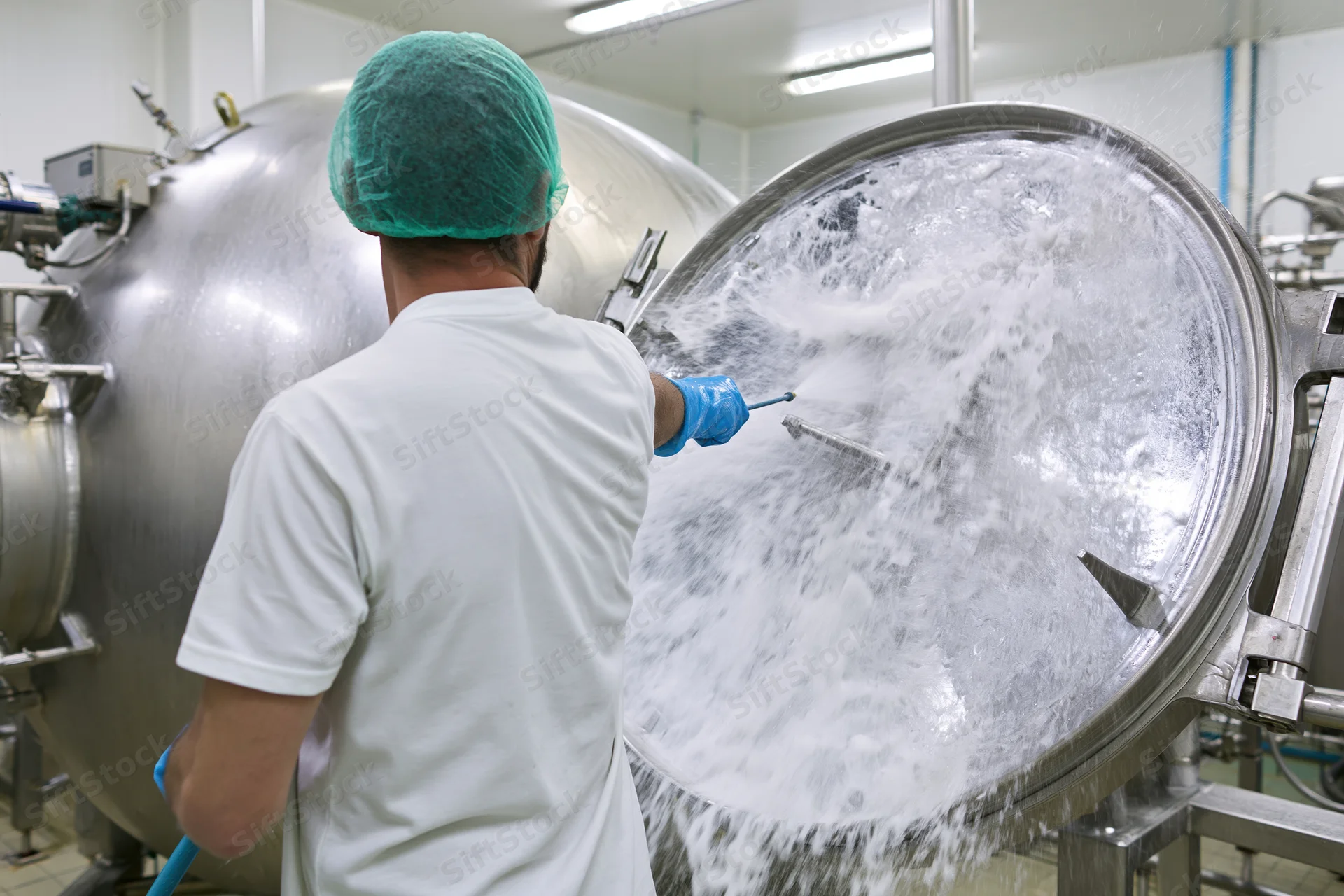 Worker cleaning large stainless steel tank in food factory interior