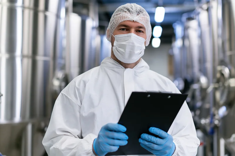 Food safety technician in white protective coveralls holding clipboard in industrial processing plant