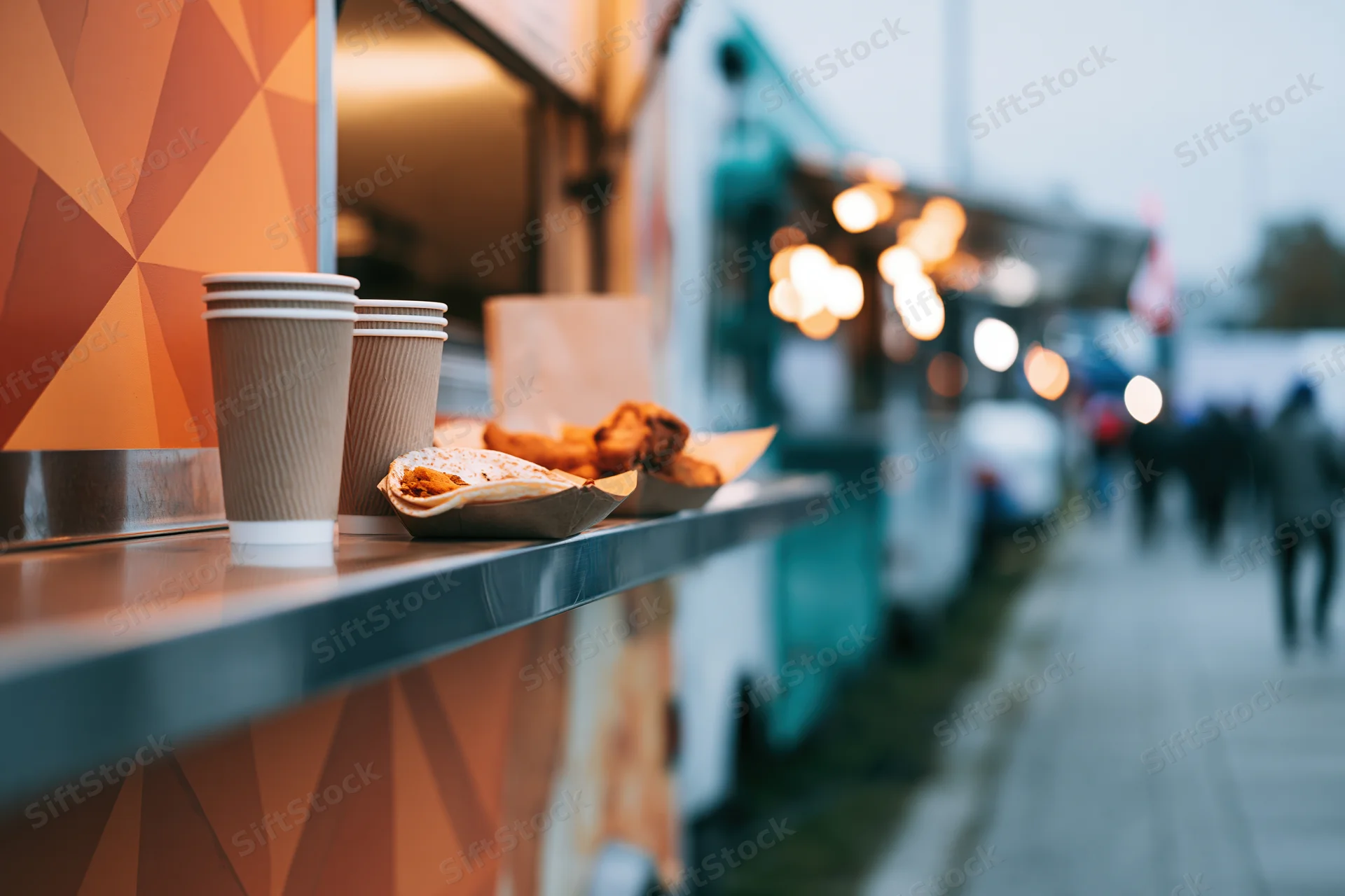 Food truck counter with paper cups and snacks on a city sidewalk at evening
