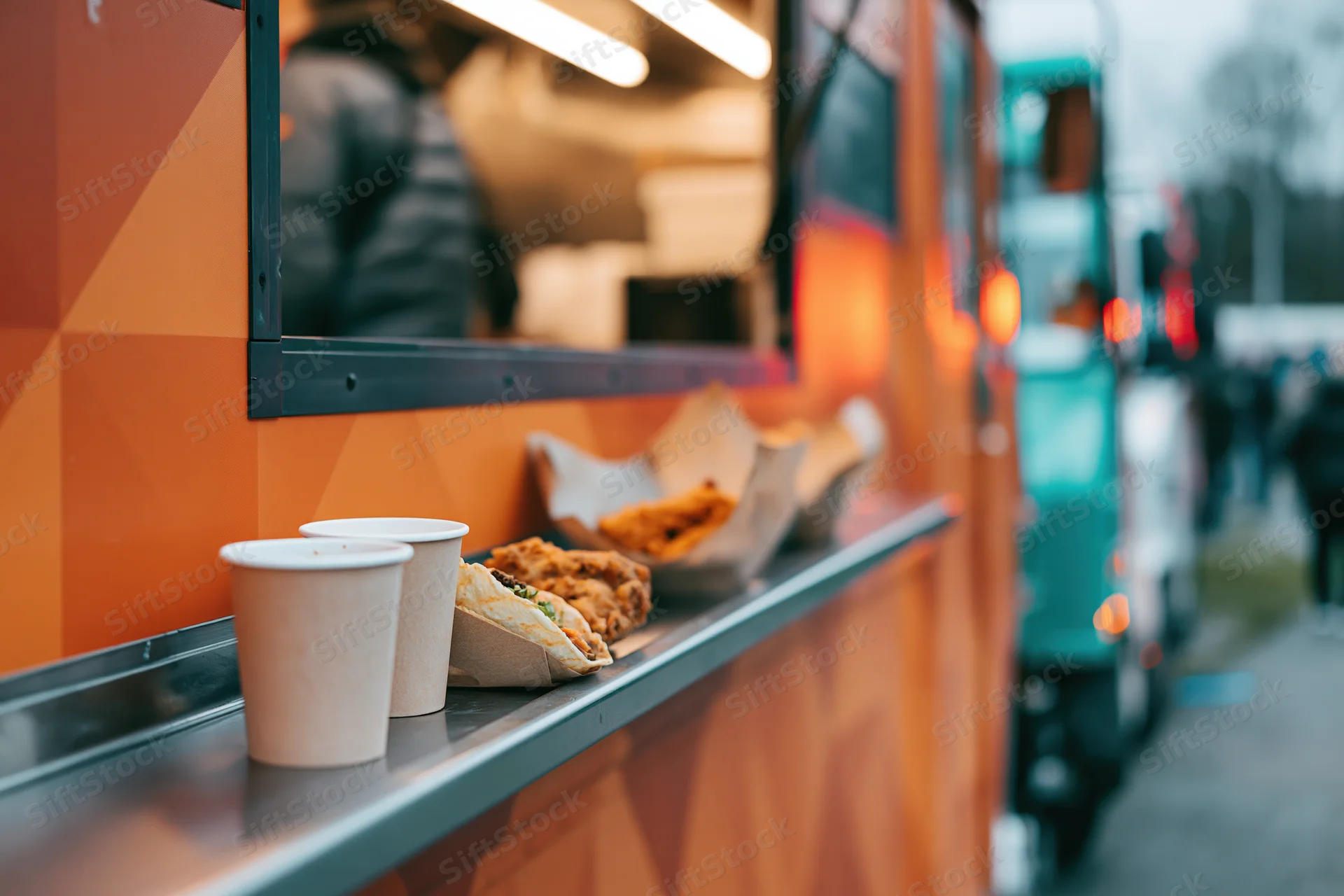 Food truck service counter with paper cups and tacos on stainless steel ledge outdoors