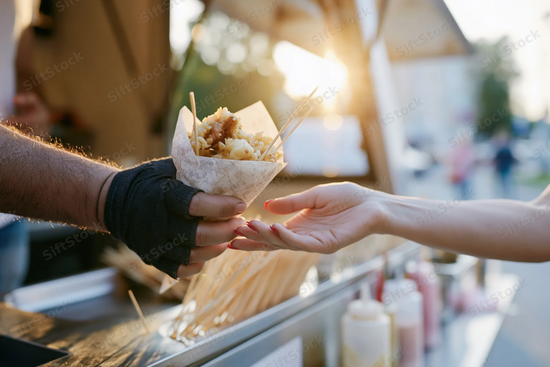 Vendor hand passing paper cone of food to customer at outdoor food truck stall